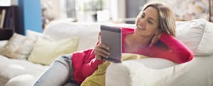 Woman sitting on sofa with digital tablet, looking up esurance auto insurance