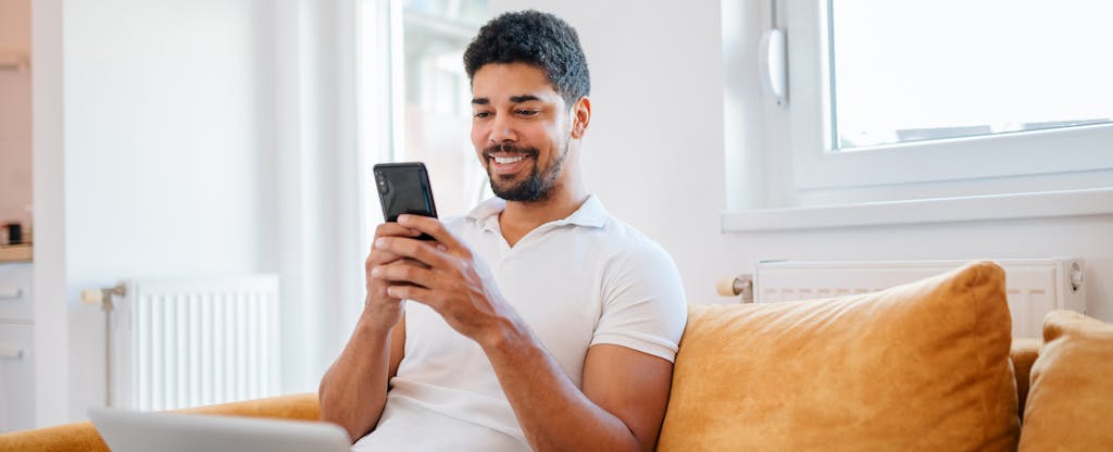 Man sitting on sofa at home with cellphone, looking up how to save money