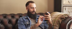 Young man sitting on couch at home, looking up what is a bad credit score on his cellphone