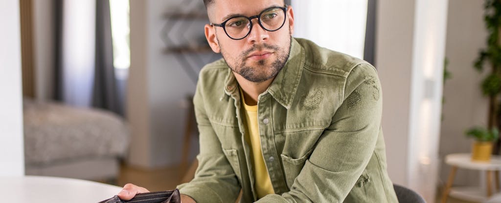 Young man sitting at home with an empty wallet.