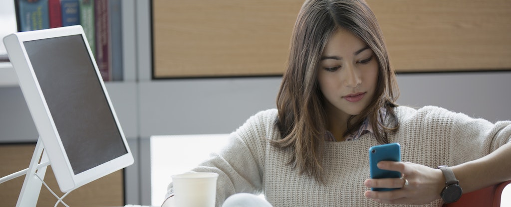 Woman sitting at her desk at work, reading a CareCredit review on her phone