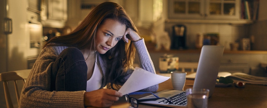 Woman sitting at her kitchen table with her laptop open, reading through her credit report and learning about LVNV funding