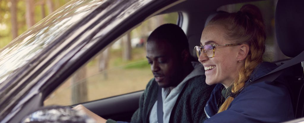 Woman driving a car with her partner in the front seat, smiling as they discuss their Metromile Insurance coverage