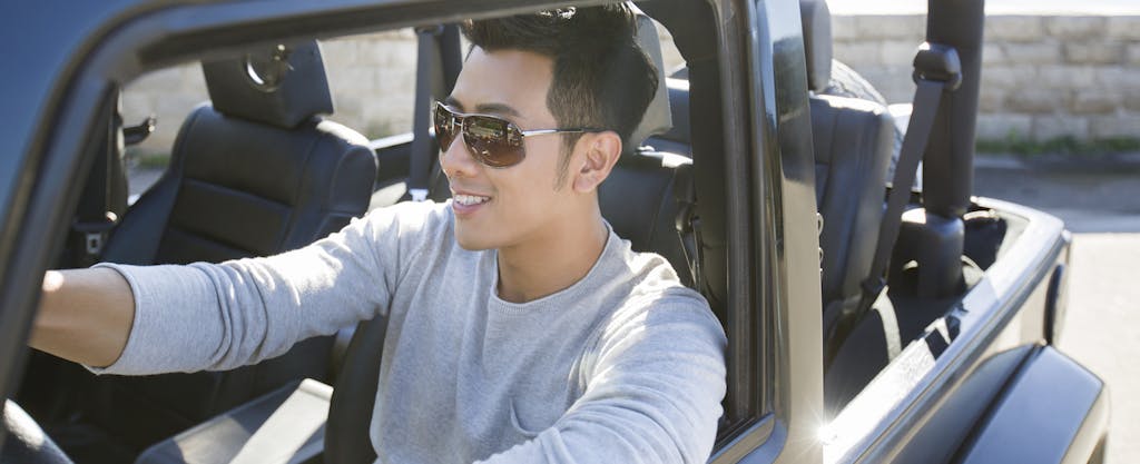 Young man wearing sunglasses and driving his Jeep with the top down