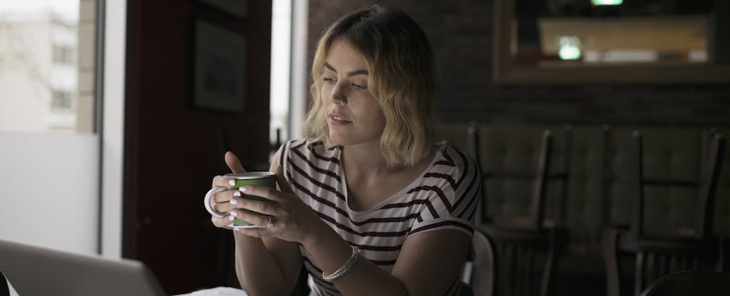 Woman holding a cup of coffee in a dimly lit room, wondering how to get a car back after repossession
