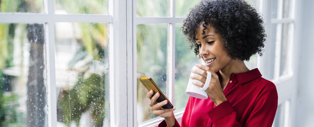 Woman at home drinking cup of coffee and looking up the 2020 standard deduction on her cellphone