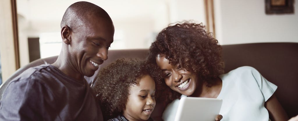 Smiling parents looking at son using digital tablet in living room as they talk about how to make an offer on a house