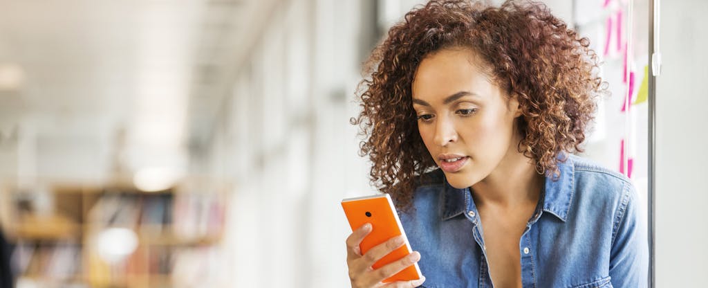 Woman looking at cellphone to read about the consequences of depositing a fake check