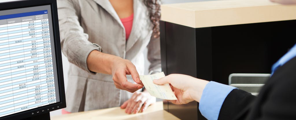A woman hands a check to a bank teller