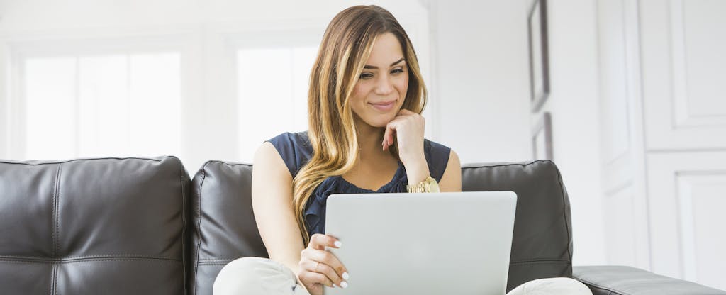 Woman on couch looking at laptop, figuring out how much money to keep in her checking account