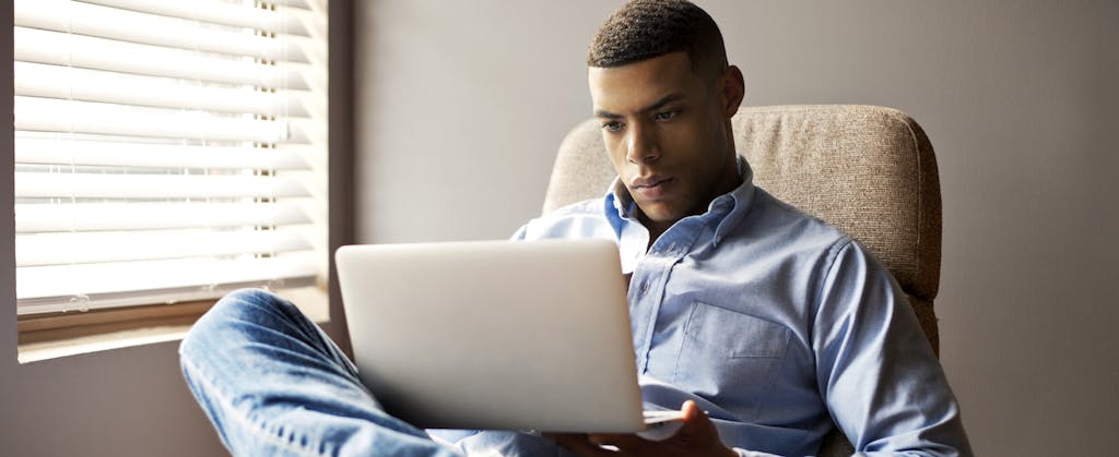 Young man sitting at home, using his laptop to read about wire transfer fees