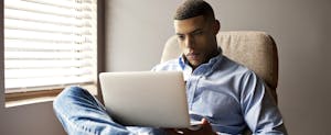 Young man sitting at home, using his laptop to read about wire transfer fees