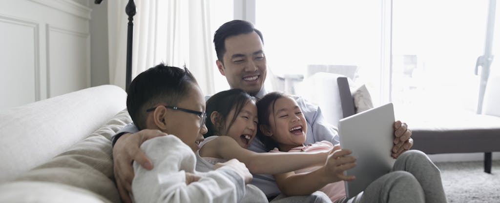 Father and young children taking on a sofa, playing educational math and finance games on a digital tablet