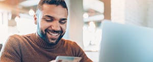 Smiling young man holding a credit card and using laptop to look up buy now pay later apps