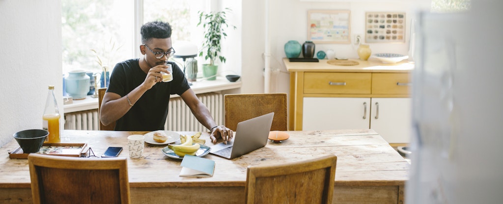 Man sitting at home, eating breakfast and reading on his laptop about cash management accounts