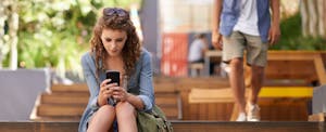 Young woman sitting on steps outdoors and looking at her cellphone.