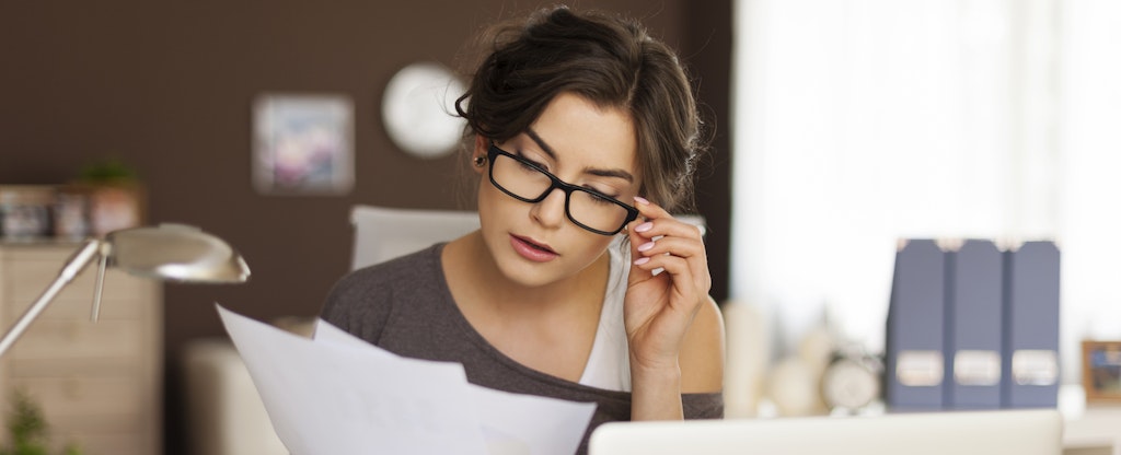 Young woman with glasses on at her desk, looking at her budget and financial paperwork