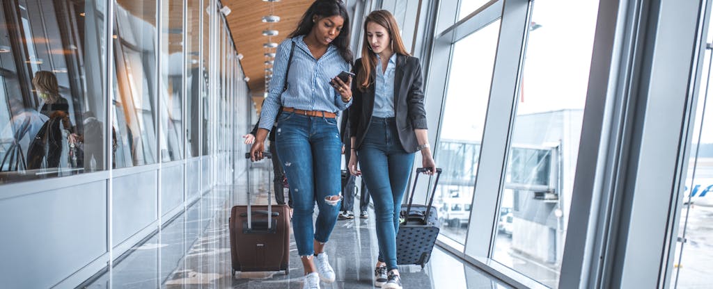 Two women with suitcases walking through airport and talking