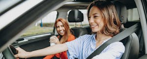 Two smiling women driving with car windows rolled down