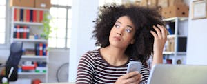 Pensive young woman holding smart phone at workplace.