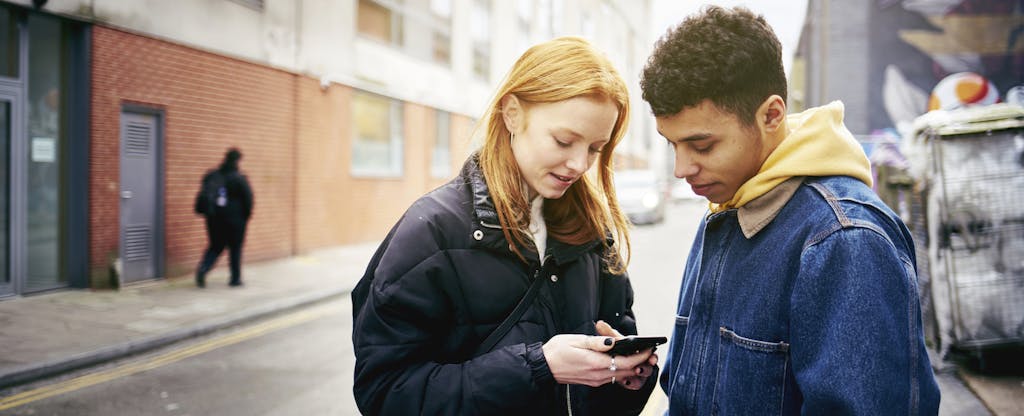 Young woman and man standing together on the street, reading on a phone about Experian vs. Credit Karma