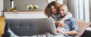 Man and woman sitting at home together, sitting on the couch and reading on their laptop about VA loans