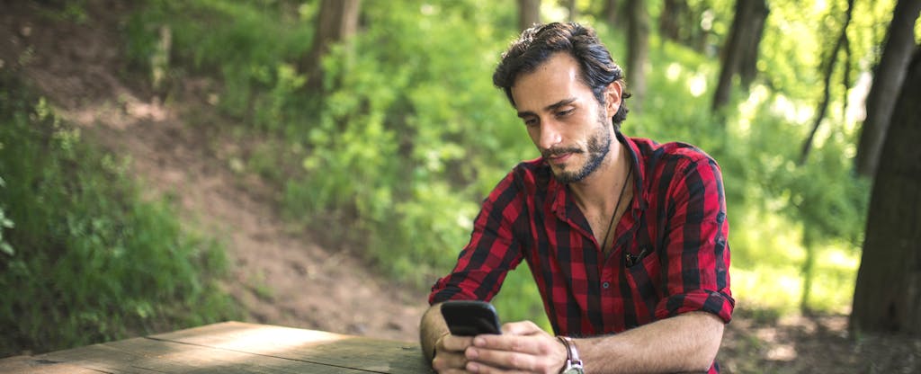 Young man using a phone while sitting in the park