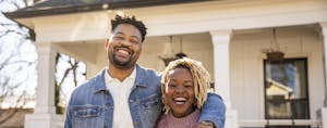 Smiling couple in front of their new home, financed by Navy Federal Credit Union