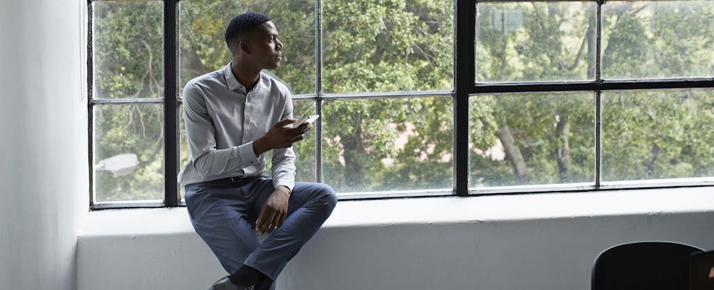Young professional man sitting next to window, searching for checking account number on phone