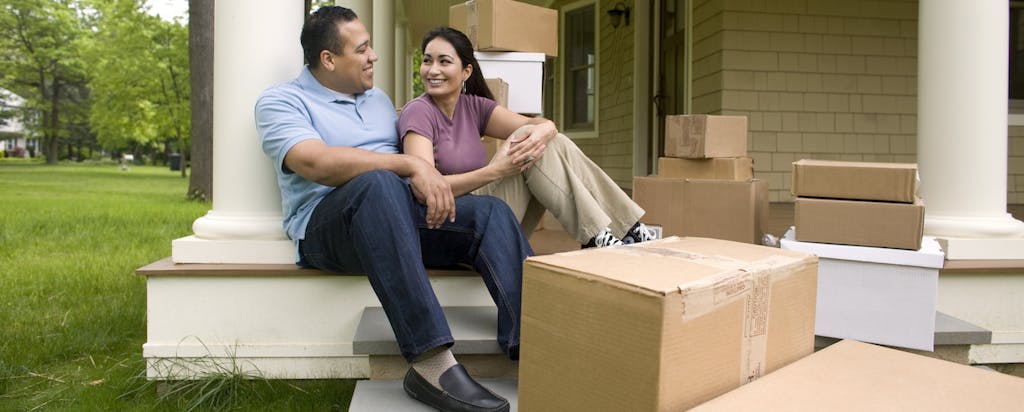 Couple resting on front porch of new home surrounded by moving boxes