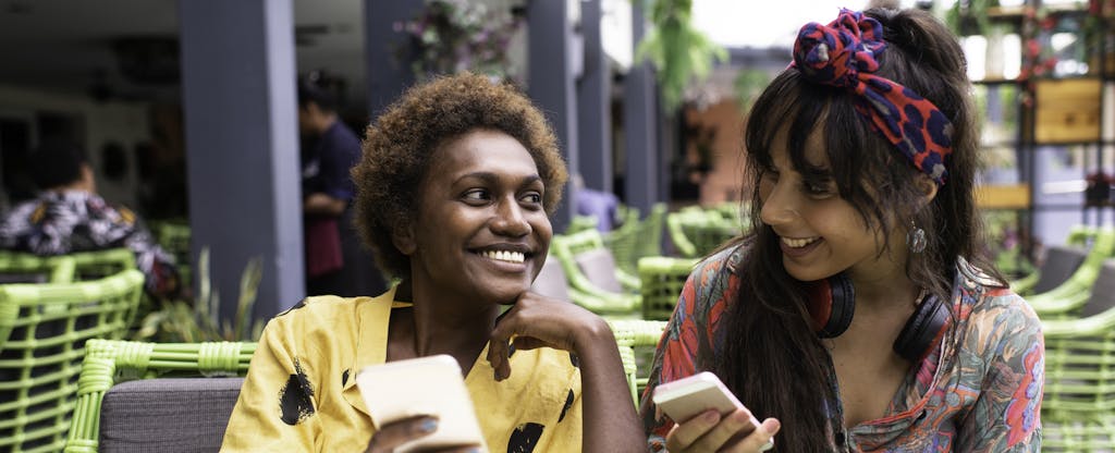 Two smiling women compare cash advance apps like MoneyLion on their phones.