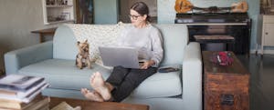 Woman on a couch at home with her laptop and dog