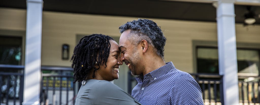 Smiling couple embraces in front of their new home.