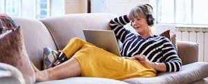 Woman with a prosthetic leg reclines on a sofa and researches conventional loan vs. FHA loans on a laptop.