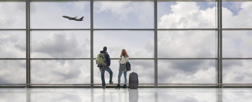 Young couple at airport, looking out through the windows as a plane takes off.