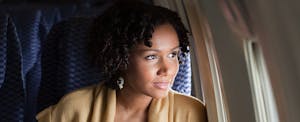 Young black woman enjoying her Frontier status perks, gazing out the plane window.