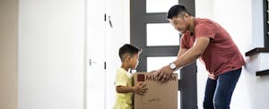 A father helps his young son lift a box as they move into their new home.