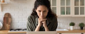 A woman seated in her kitchen researches a no-closing-cost refinance on her laptop.