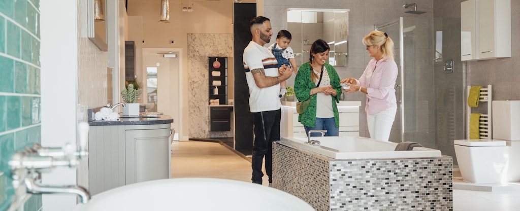 A sales representative assists a young couple as they look at bathtubs in a showroom.