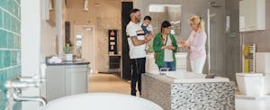 A sales representative assists a young couple as they look at bathtubs in a showroom.