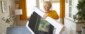 A person smiles as they lift a new flat screen tv out of its box.