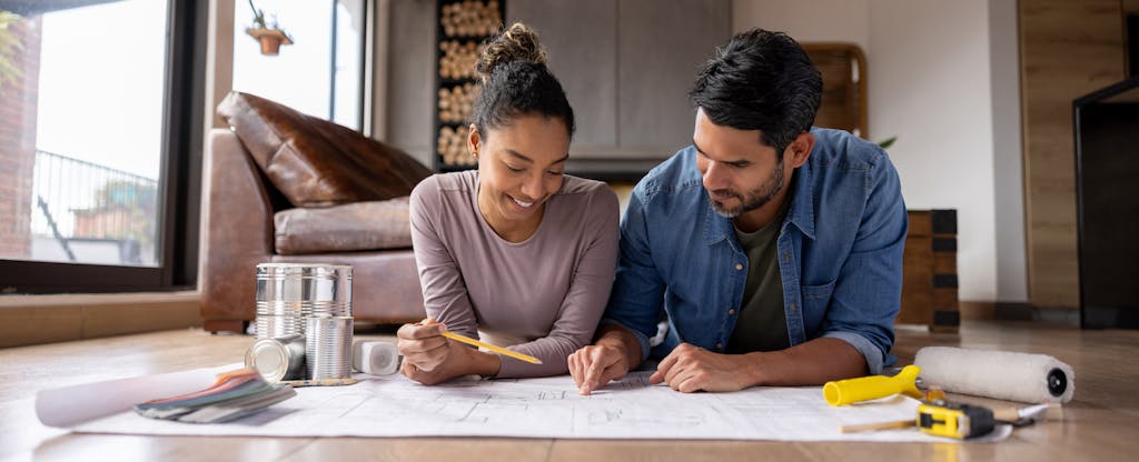 A couple lying on the floor review a blueprint of their new home addition together.