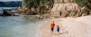A father and small child walk along a beach in the sunshine.