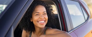 Young women smiles while looking outside car from driver's seat