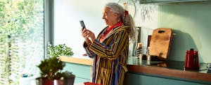 A smiling person with long gray curly hair uses their smartphone to open a Discover checking account.