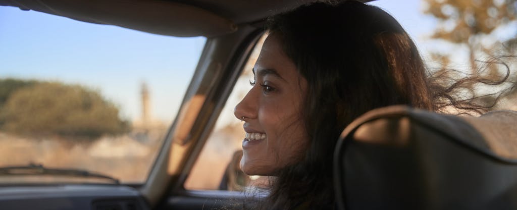 Woman smiling in the passenger seat of a car as they drive through a picturesque location