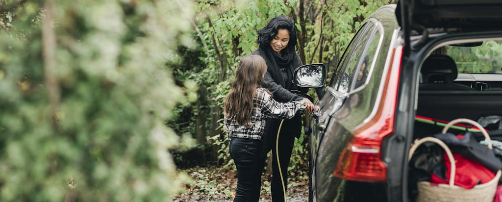 Woman with her daughter charging her electric vehicle in a woodsy area