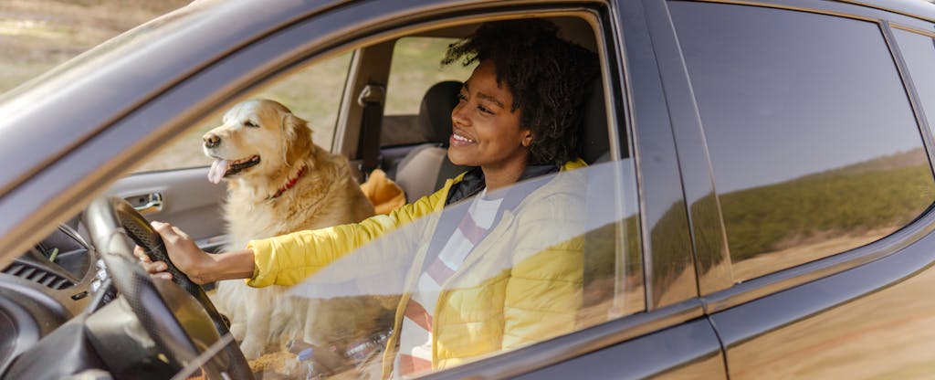 A smiling person sits in the driver's seat of a car with their dog in the passenger's seat.
