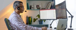 An actuary wearing a headset sits at his desk in front of two computer monitors and a laptop.