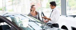 A salesman shows a young woman a new car at a dealership.